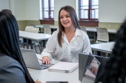 Woman student with laptop and notebook chatting with fellow students off-camera