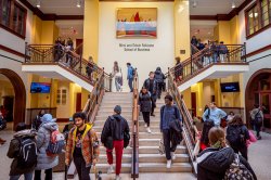 Wide view of the Feliciano School of Business building's lobby with dozens of students going up and down the grand staircase.