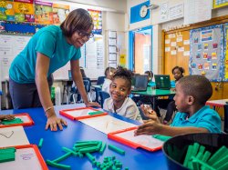 An Urban Teacher Residency student helps elementary school children with math using counting blocks.