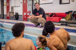 Students in a pool listen to an instructor.