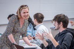 Professor leaning over desk, talking to student in lecture hall