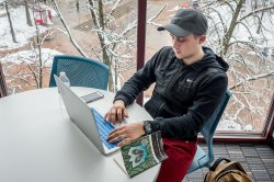 A student uses a laptop in a lounge in front of a large window overlooking the main quad in winter