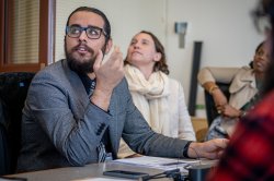A student wearing a blazer looks up at the projector screen and makes a gesture while asking a question