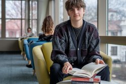 A student sits by the window in the library with a stack of books including Gay Macho by Martin P Levine and The remarkable Rise of Transgender Rights by Jami K Taylor, Daniel C Lewis, and Donald P Haider-Markel