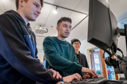 Two students controlling a prototype game using a keyboard while a third looks on