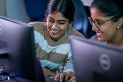 Two students smiling while looking at a computer monitor in a computer lab