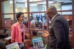 Student in business attire stands behind a table at a pitch competition, speaking to a business professional