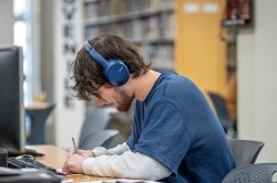 Student with headphones sitting at a computer in the library