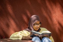 Student wearing a hijab and reading a book in the shade
