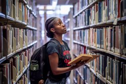 Person standing in library aisle holding an open book