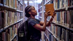 A student in the library pulls a book from the shelves and checks its spine.