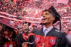 students smiling at graduation ceremony wearing caps and gowns as confetti falls