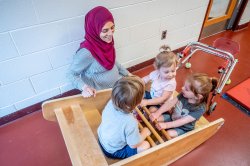 A teacher helps a group of young students in a toy rowboat.