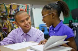 An elementary school teacher helps a student read a book.