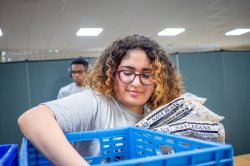 A student volunteer packs bags of navy beans into a crate.