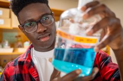 A student in a lab holding a glass flask holding a blue liquid