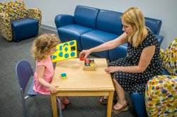 Sitting at a low table, a woman and a young girl play with colored blocks.