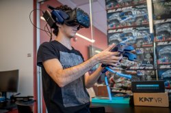 Student using VR headset with two controllers in front of a wall of remote controlled cars.