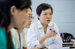Three people sitting at desks, one person speaking with pen in hand
