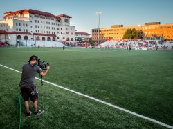 Student with camera on the sidelines of a soccer pitch