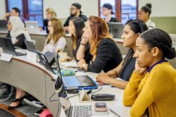 Two rows of students in a classroom with the desks arranged in tiers to make an amphitheater-style presentation space
