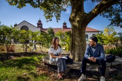 two students conversing on a bench under tree shade on Montclair campus
