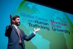 Montclair State University President Jonathan Koppell stands on stage in front of a large screen displaying a world map and the words "Global Center on Human Trafficking" and "Montclair State University."