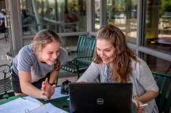 Two students talking over a laptop, notebook in the foreground with French translations