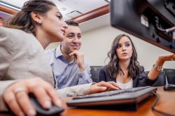 three students talking in front of computer monitor