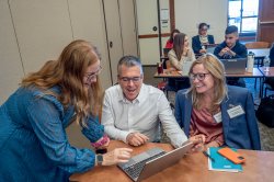 A university professor shows adult learners an assignment on a laptop in a classroom setting.