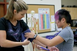 One student takes another student's blood pressure in a classroom