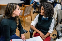 Two graduate students speaking, one holding a binder open between them