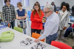 A teacher evaluates at an assignment as a group of students look on.