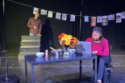 Student working on laptop, seated on a table in stage set