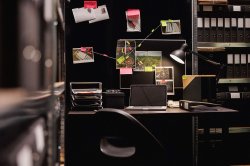 Photo of a desk in a police department with a cork board behind it with assorted photos and notes