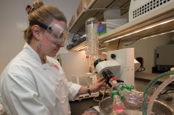 Student in chef's jacket wearing safety goggles working in the food lab