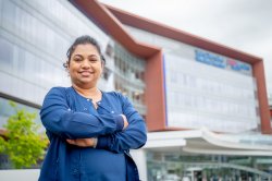 Nursing alumna Sandy Hussain in scrubs standing in front of hospital