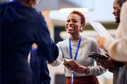 A woman in business-casual clothes wearing a lanyard shakes hands with someone off-camera