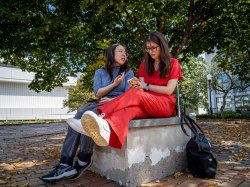 Two students siting on a stone bench as they talk.