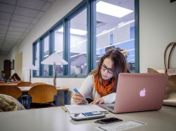 Woman student in quiet study room in the Sprague library taking notes from a laptop