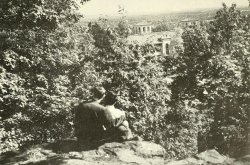 Two students sitting on rock outcropping overlooking campus
