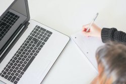 Stock photo of woman taking notes while reading off a laptop screen