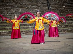 Women in traditional chinese dress dance with fans.
