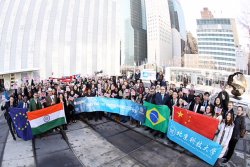 Photo of a large crowd gathered outside the United Nations building posing for photos and standing with banners and flags from a multiple nations.
