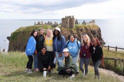 group of students smile on a hill overlooking a castle in distance