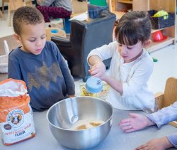 Photo of children using mixing bowls and measuring cups to make a mixture of something.