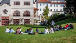students attending class outside, sitting on lawn