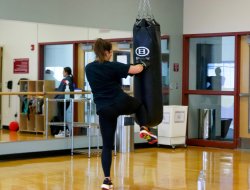A female punching and kneeing a punching bag.