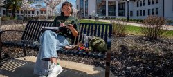 Picture of a student sitting on a campus bench working on a tablet.