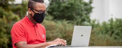 Student wearing mask using laptop on campus
